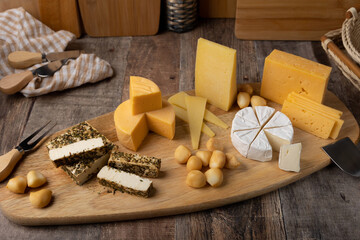 Cheese assorted on a wooden board, rustic style. Several varieties sliced cheeses: parmesan, tilsiter, halloumi with spices, camembert, smoked bocconcini, cheddar. Selective focus, close-up.