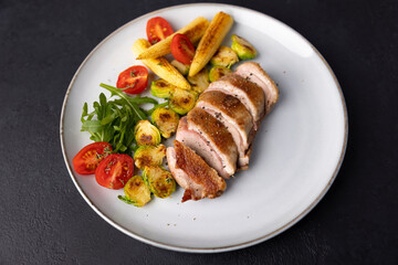 Grilled duck breast fillet with Brussels sprouts, mini corn, cherry tomatoes and arugula. Traditional Mediterranean cuisine. Selective focus, close-up.