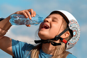 Teenage girl in fall protection drinks water from a bottle. Child quenches thirst after playing...