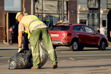 A male janitor removes garbage bags from the streets of the city. The city service takes care of...