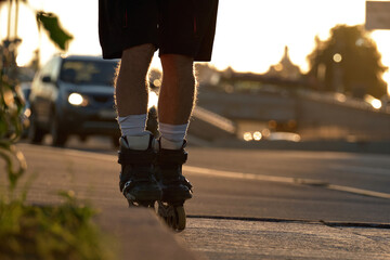 A man rides roller skates on the paved.walkway at sunset on city roads in summer. Rollers close-up...