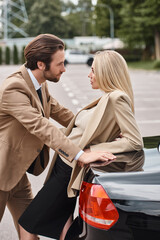 elegant man in formal wear looking at sensual blonde businesswoman near car on street, attraction