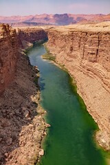 Portrait view of the Colorado River canyon in the dry, desert red rock landscape of Arizona with canyon cliffs, mountains and running river.