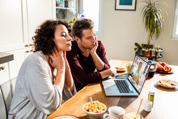 Young couple talking to their doctor over a video call on their laptop at home