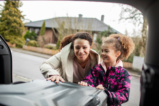 Happy mother and daughter put their suitcase in car trunk
