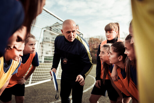 Male coach talking to female soccer team on football pitch