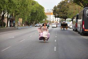 Young, Hispanic, pretty, brunette woman, wearing an elegant vintage violet dress, running funny on the road in the middle of traffic. Concept of beauty, fashion, trend, madness, escape.