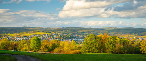 Panorama of a autumn landscape with colorful trees, the village in the valley and wind turbines on...