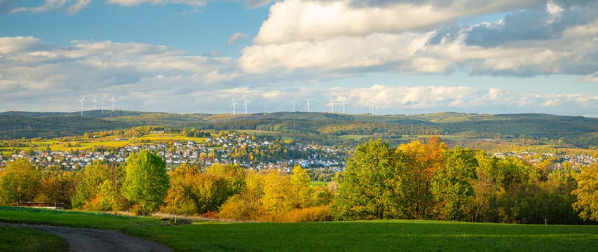 Panorama of a autumn landscape with colorful trees, the village in the valley and wind turbines on the hilltop