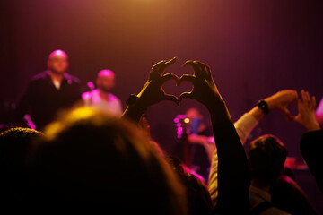 A crowd of people at a concert making heart shapes with their hands.