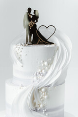 Two tier wedding cake with white chocolate frosting decorated with bride and groom couple...
