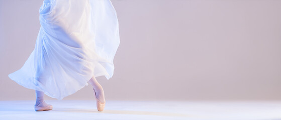 The legs of a ballerina in pointe shoes stand under a developing flying skirt on a white background
