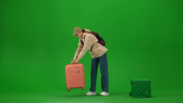 Portrait of traveler isolated on chroma key green screen background. Young girl puts heavy suitcase on the ground takes out holder walks away
