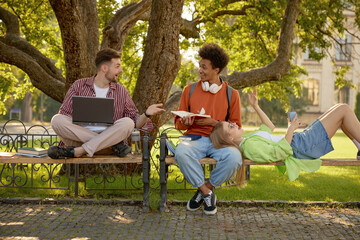 Students communicating while sitting together on park bench