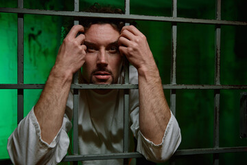 Portrait of young man with mental disorder behind cage-ward door