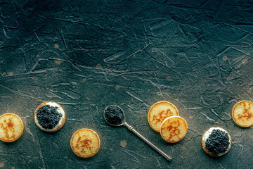 Blinis with black caviar and cream cheese, top shot on a black stone background, mini pancakes,...