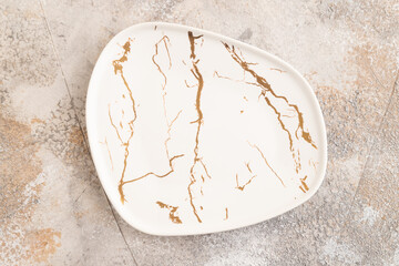 Empty white and gold ceramic plate on brown concrete background. Top view, copy space