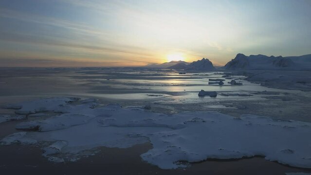 Dawn over Antarctic coast. Polar night sunset. Ocean covered ice. Top above aerial view. Antarctica snow mountain. Sky sunrise Antarctica winter. Open water. Beautiful sky landscape. Top Drone Flight