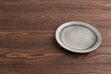 Empty gray ceramic plate on brown wooden. Side view, copy space
