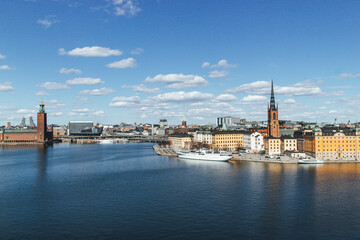 panoramic view of rooftops and view of the town hall tower with many colorful houses in stockholm and water channels huge boat and cloudy sky