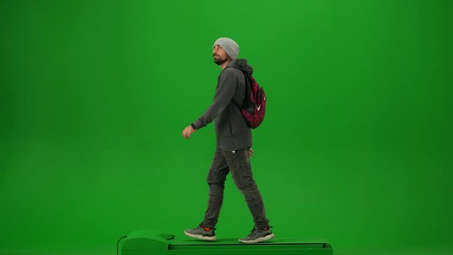 Portrait of traveler isolated on chroma key green screen background. Young man with backpack in knitted hat walking and looking around.