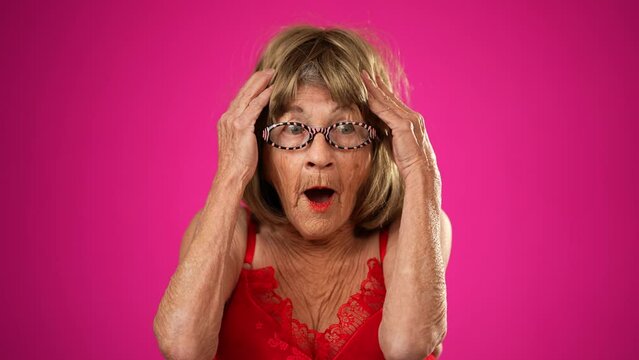 Portrait of funny elderly senior old woman with no teeth and wrinkled skin looks at camera has great idea gesture showing explosion of thinking posing isolated on pink background