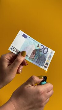 Paper money collapse, replacing currency, finance concept. A female hand holds a banknote, igniting Euro note as it gracefully burns indoors. Vertical video isolated on yellow or orange background