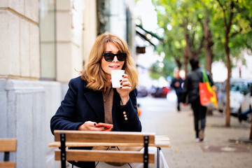 Blond haired businesswoman sitting at the table at outdoor cafe and drinking coffee