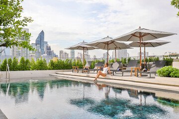 Woman relaxing by pool in luxurious urban rooftop setting. Urban relaxation and lifestyle.