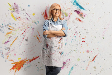 Happy middle aged woman with an artist apron leaning on wall