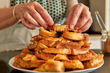 Close up of senior woman hands stacking easter and lent dessert. Traditional spanish recipe of torrijas or torrejas
