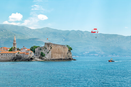 Flight on a parachute behind a boat against the backdrop of the ancient fortress of the Old Town of Budva, Montenegro. Extreme entertainment for tourists in the Budva Riviera in summer