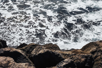 Rocky shore background. Volcanic rock on ocean shore. Tenerife on Canary island landscape. Sea wave crushing. Water white foam. Turbulent ocean background.