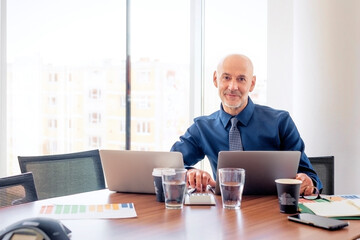 Mid aged businessman sitting in a modern office and using laptops for work