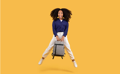 Excited black student lady with backpack jumping on a yellow background