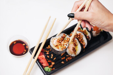 Takeaway sushi background. Woman hand holding chopsticks. Sushi roll sprinkled with sunflower seeds. Japanese food isolated on white. Soy sos in plastic container.