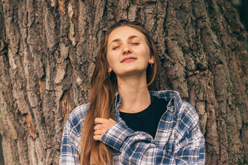 Portrait of a young attractive.long-haired woman leaning against a tree trunk on a summer day.Self-care,healthy lifestyle,leisure activity,mental health concept.