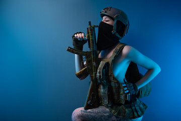 sexy girl soldier in a helmet, armed with an automatic rifle, in military clothes on a blue...