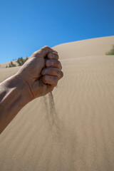Sand is falling from a man's hand against the background of a singing dune in Kazakhstan.