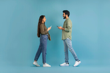 Side view young indian couple using smartphones and walking