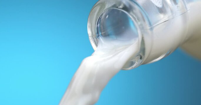 Super slow motion macro of fresh organic bio milk is being poured from transparent glass bottle with splashing white drops isolated on soft light blue background at 1000 fps.