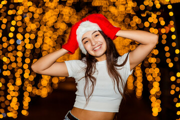 A young, beautiful girl walks in a Santa hat, in the evening city, decorated with New Year's lights