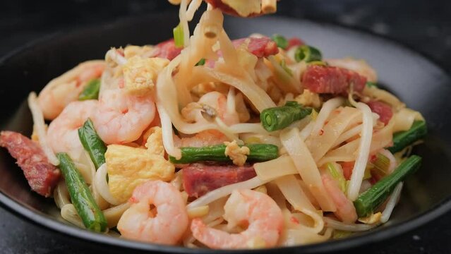 Eating Char kway teow with rice noodles, prawn, sausage, egg and vegetables.