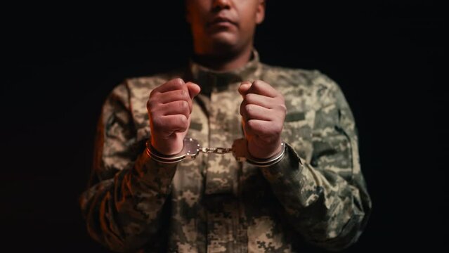 Close-up of male soldier in handcuffs on black background, military tribunal