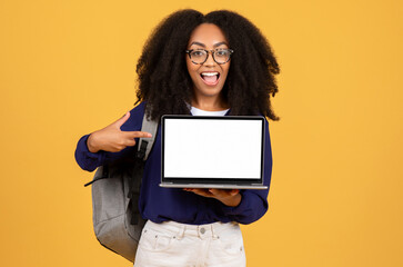 Excited black lady student pointing to laptop screen on yellow backdrop