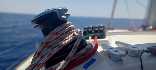 Cuerdas y cabos marineros de velero con mar azul de fondo, horizonte. Primer plano de una cuerda náutica gruesa enrollada en un cabrestante de barco, con el mar azul de fondo.