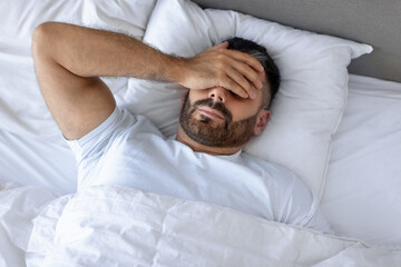 Fototapeta na wymiar man in bed covering face struggling with headaches at bedroom
