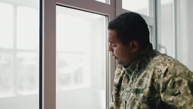 African American soldier looking out the window, worried about future, problems