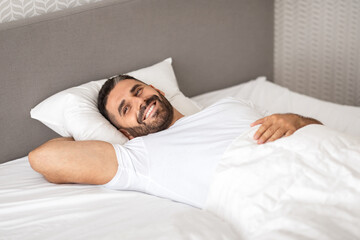 Relaxed European man happily lounging in comfortable bed in bedroom