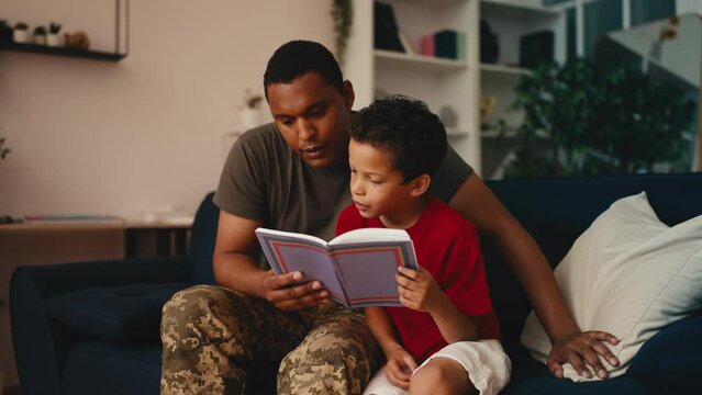 African American soldier reading a book with his little son, family time, joy